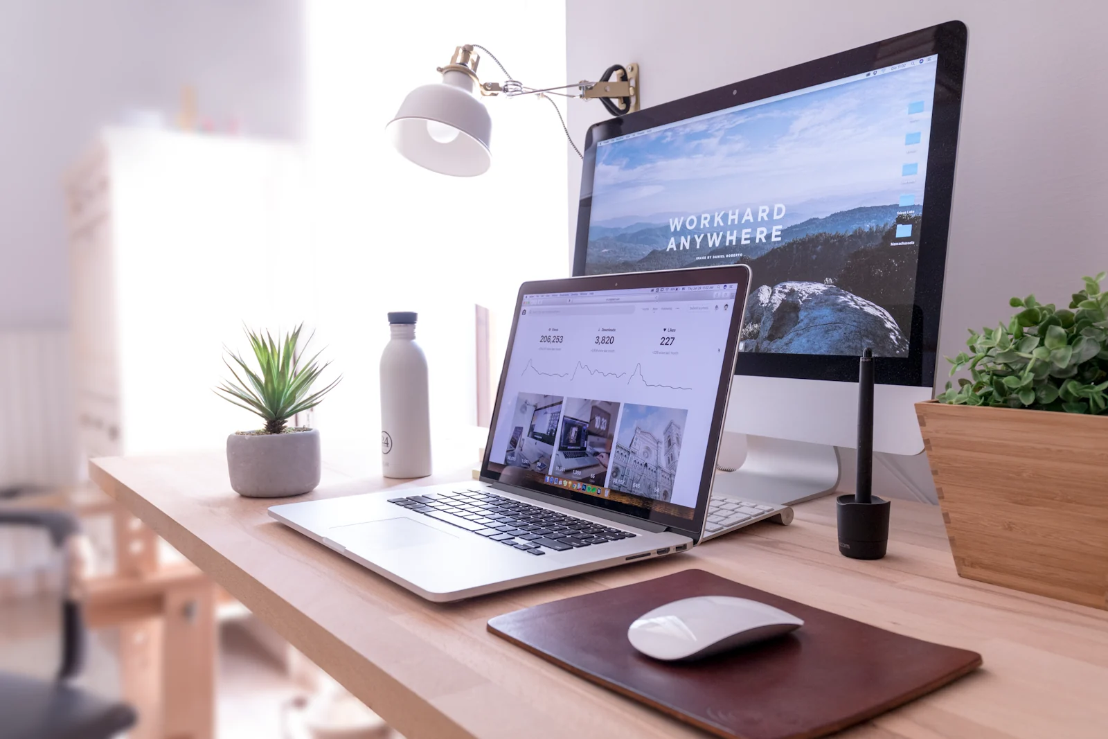 A bright creative workspace with a laptop, desktop display and plants