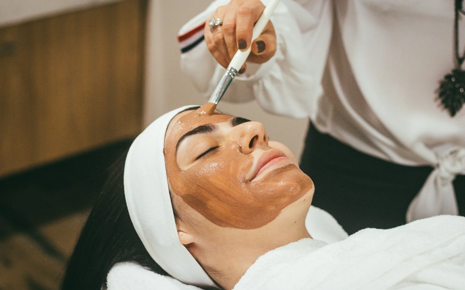 A professional applying a facial treatment with a skincare brush