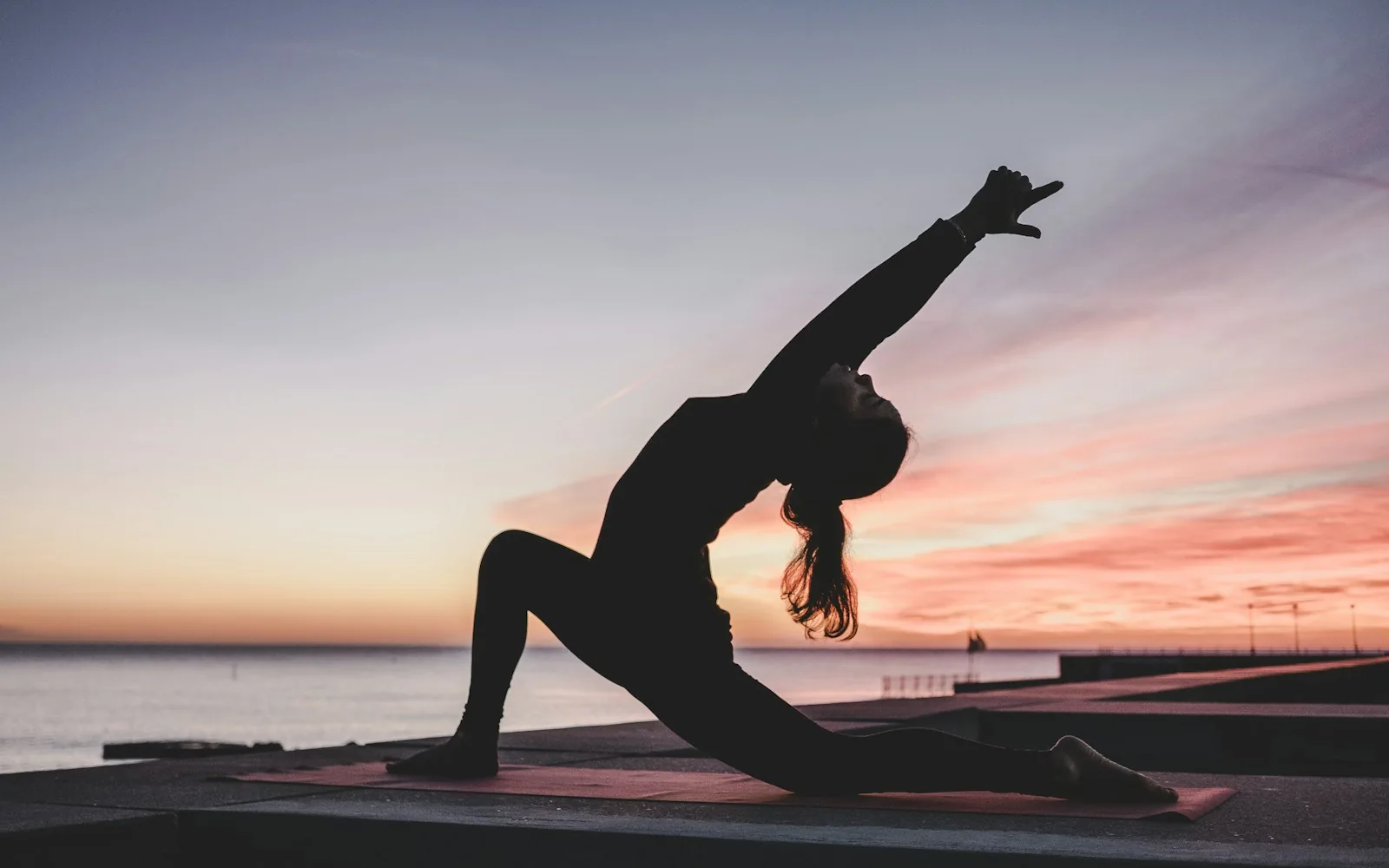 A yoga practitioner stretching beside the water at sunset
